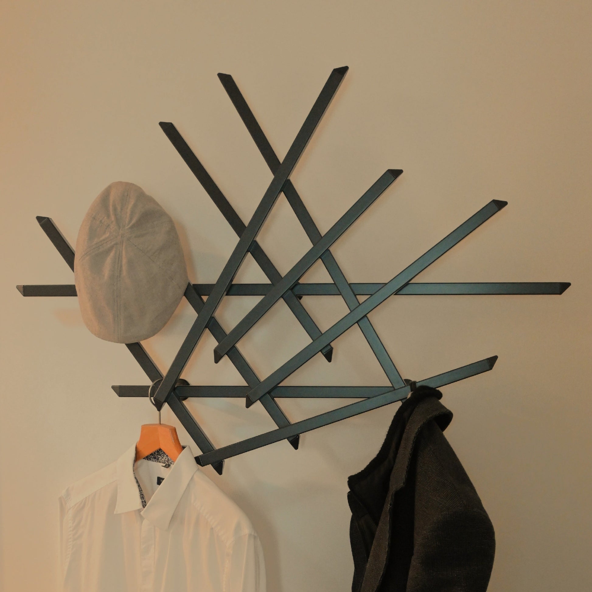 Treecado Designer-Wandgarderobe aus Aluminium in Anthrazitgrau (RAL7016), stilvoll an einer hellen Wand montiert, frontal fotografiert und mit Mantel, Hemd und Mütze behangen. Modernes, minimalistisches Design made in Germany.