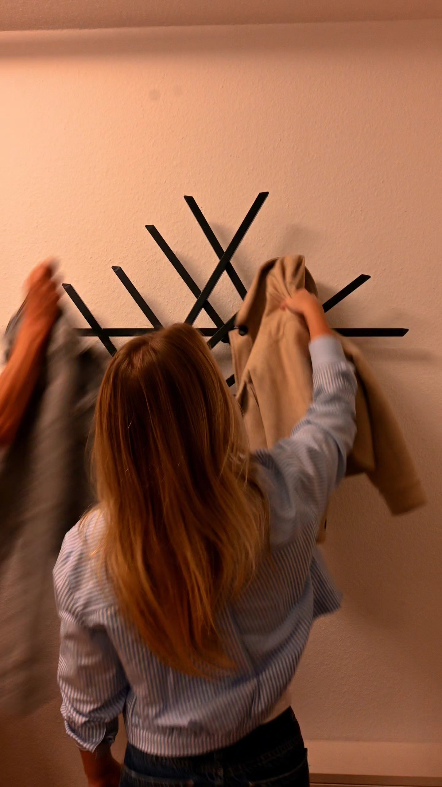 Drei Besucher betreten den Flur und hängen ihre Jacken an die Treecado Wandgarderobe. Das moderne, anthrazitfarbene Designobjekt ist an einer hellen Wand montiert und zeigt, wie einfach Kleidung aufgehängt werden kann.